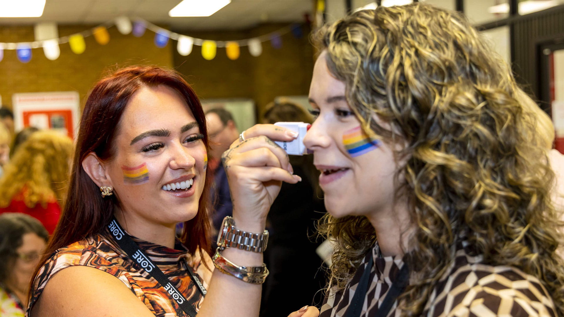 A woman applies Pride-themed face paint to another woman