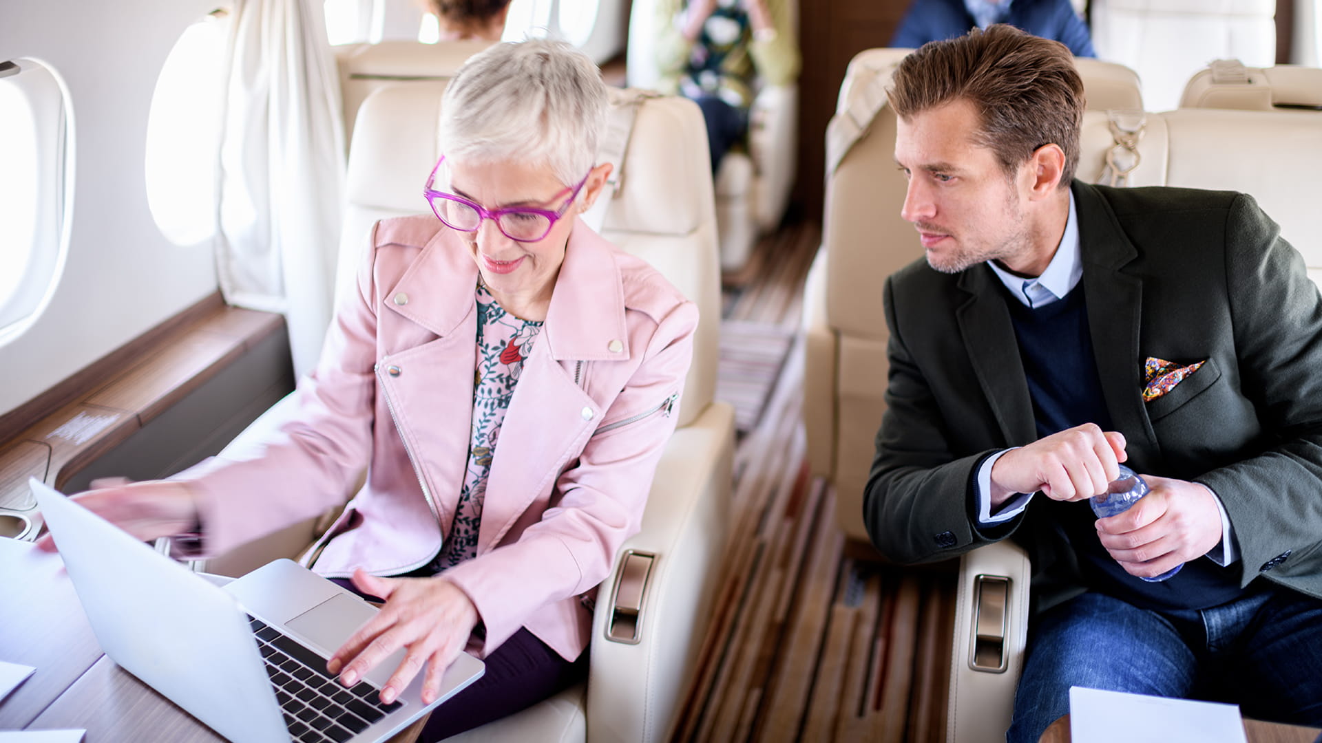 A woman operating a laptop while a man looks on. They are passengers on a private jet.