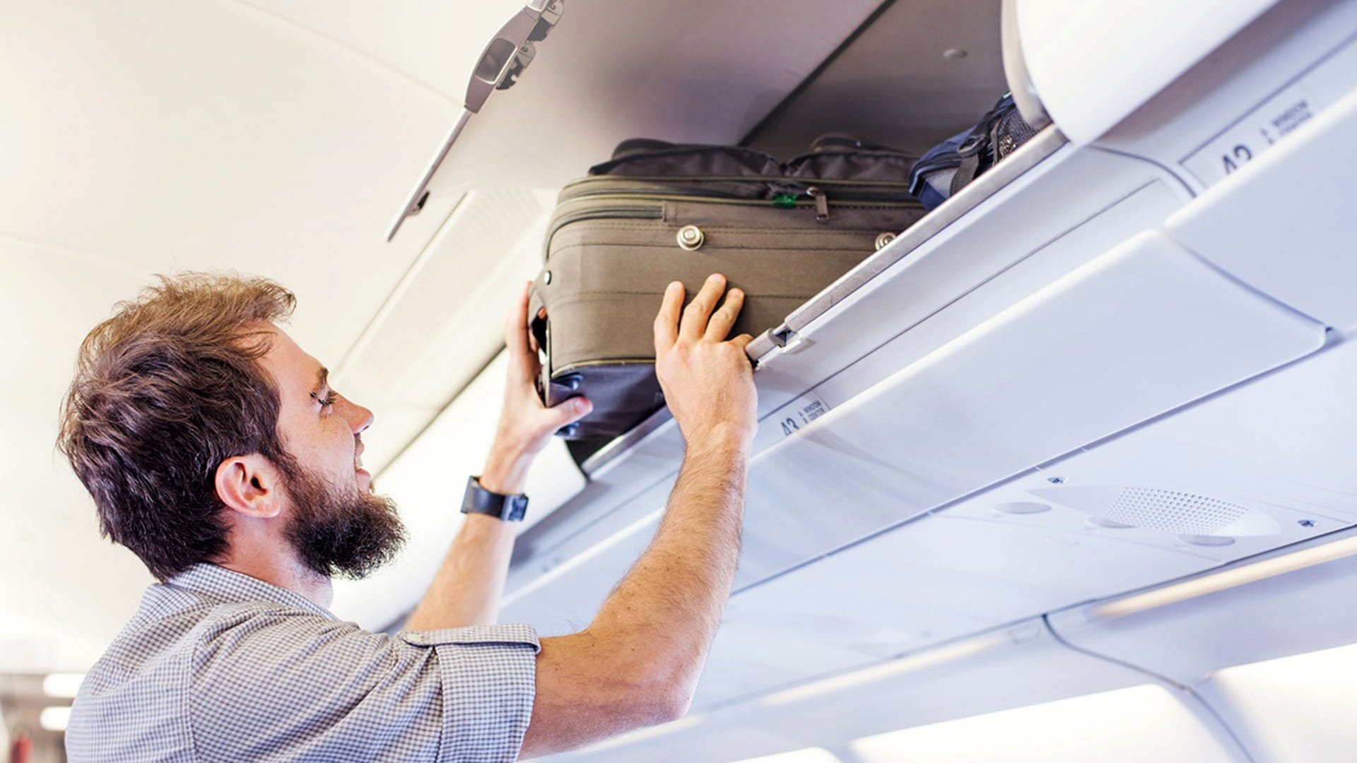 Man putting luggage in overhead bin on airplane