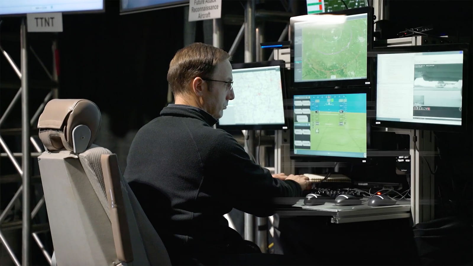 A man sits at a computer terminal while viewing four computer monitors