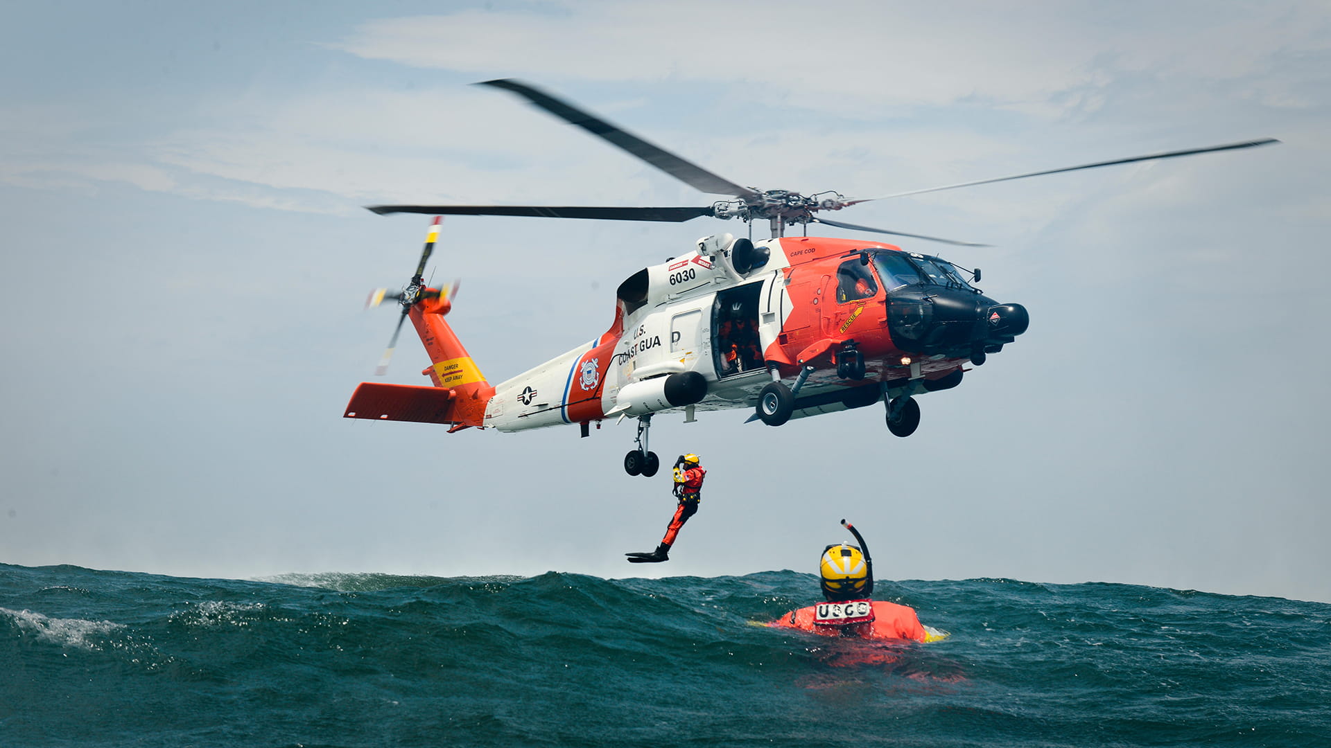 A rescue diver hangs from an MH60 rescue helicopter