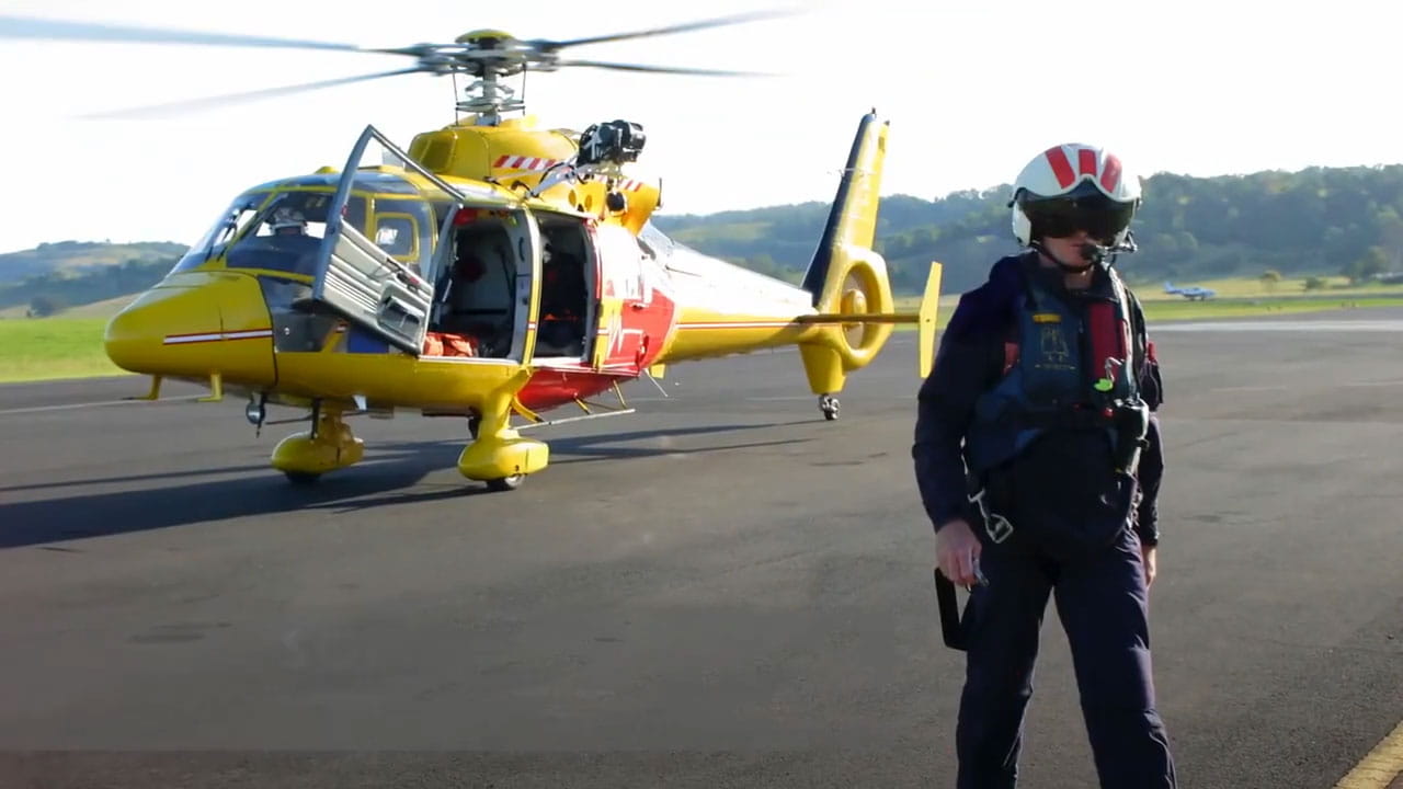 A helicopter sits on the ground with a pilot in front of it