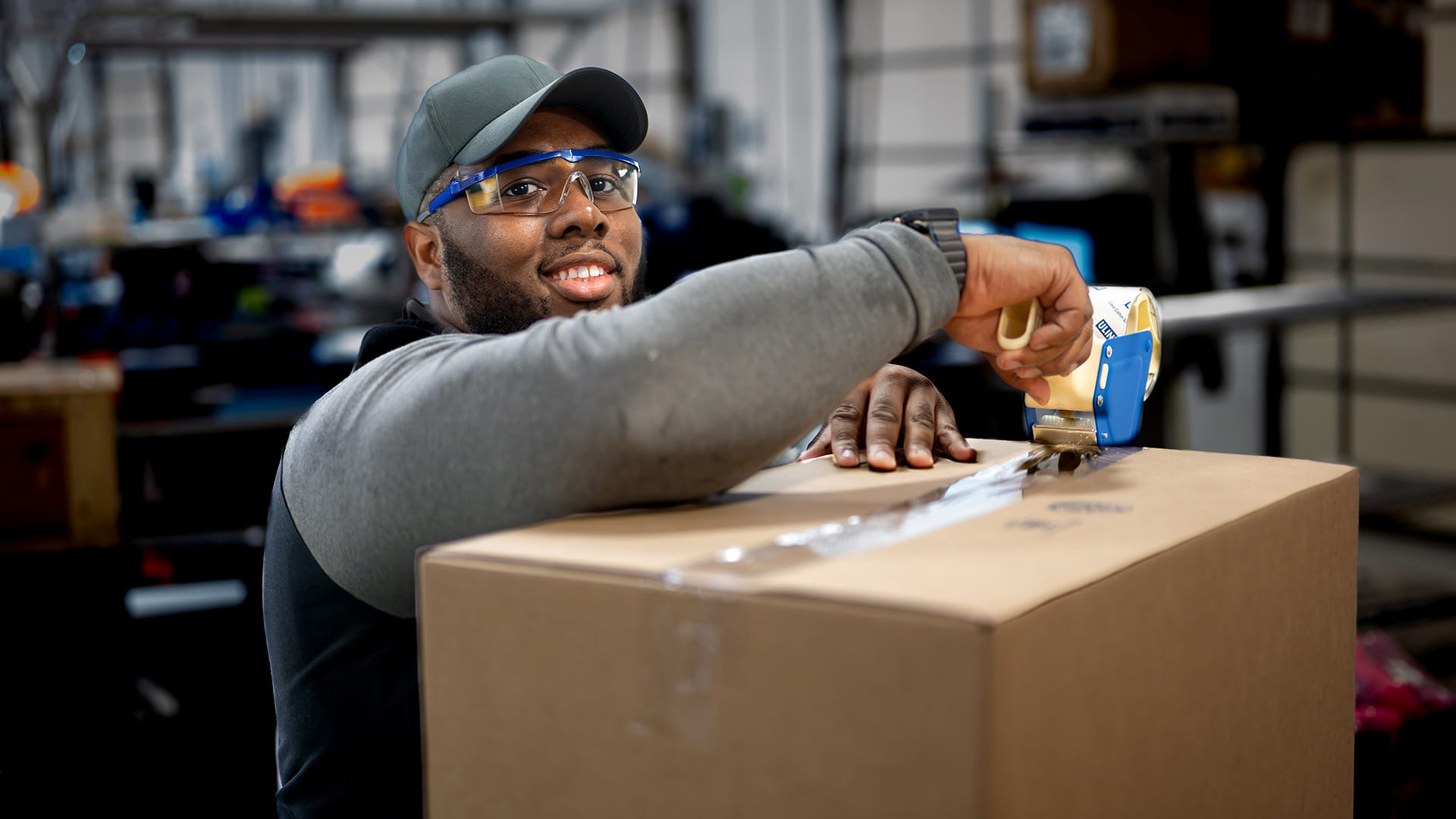 Employee with safety glasses using backing tape to seal a box