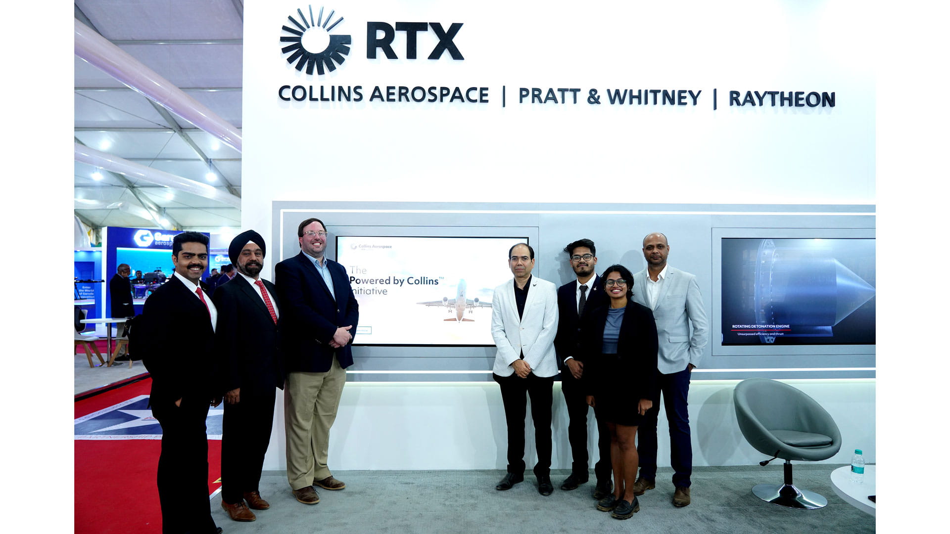 Six men and one woman stand in front of a display promoting the Powered by Collins Initiative