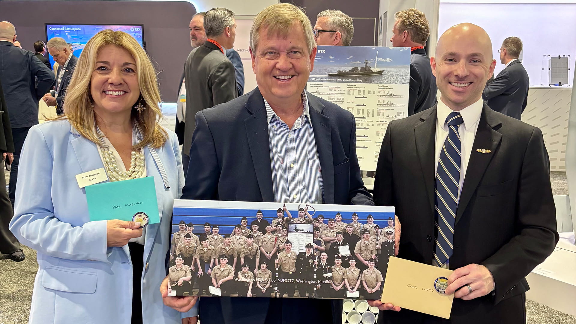 Left to right: Pam Marshall, RTX trade show lead; Retired Rear Admiral Jeffery Scott Jones; and Cory Lloyd, the Raytheon test architect responsible for annual updates to the poster. 