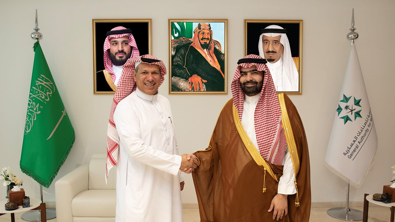 Shaking hands in front of KSA and GAMI flags