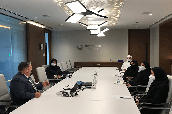 Several interns sit in conference room with business leader. 