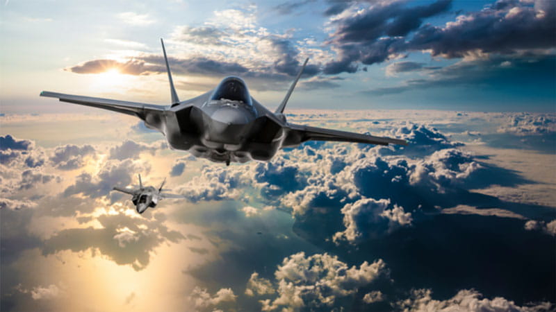 fighter aircraft flying high in a cloudy blue sky
