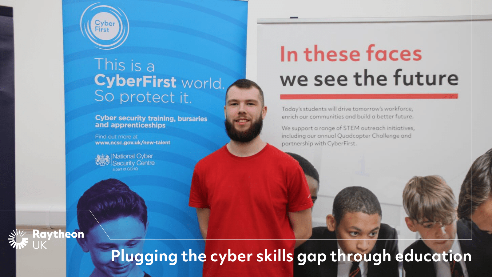 A man in a red t-shirt stands in front of a CyberFirst Schools banner