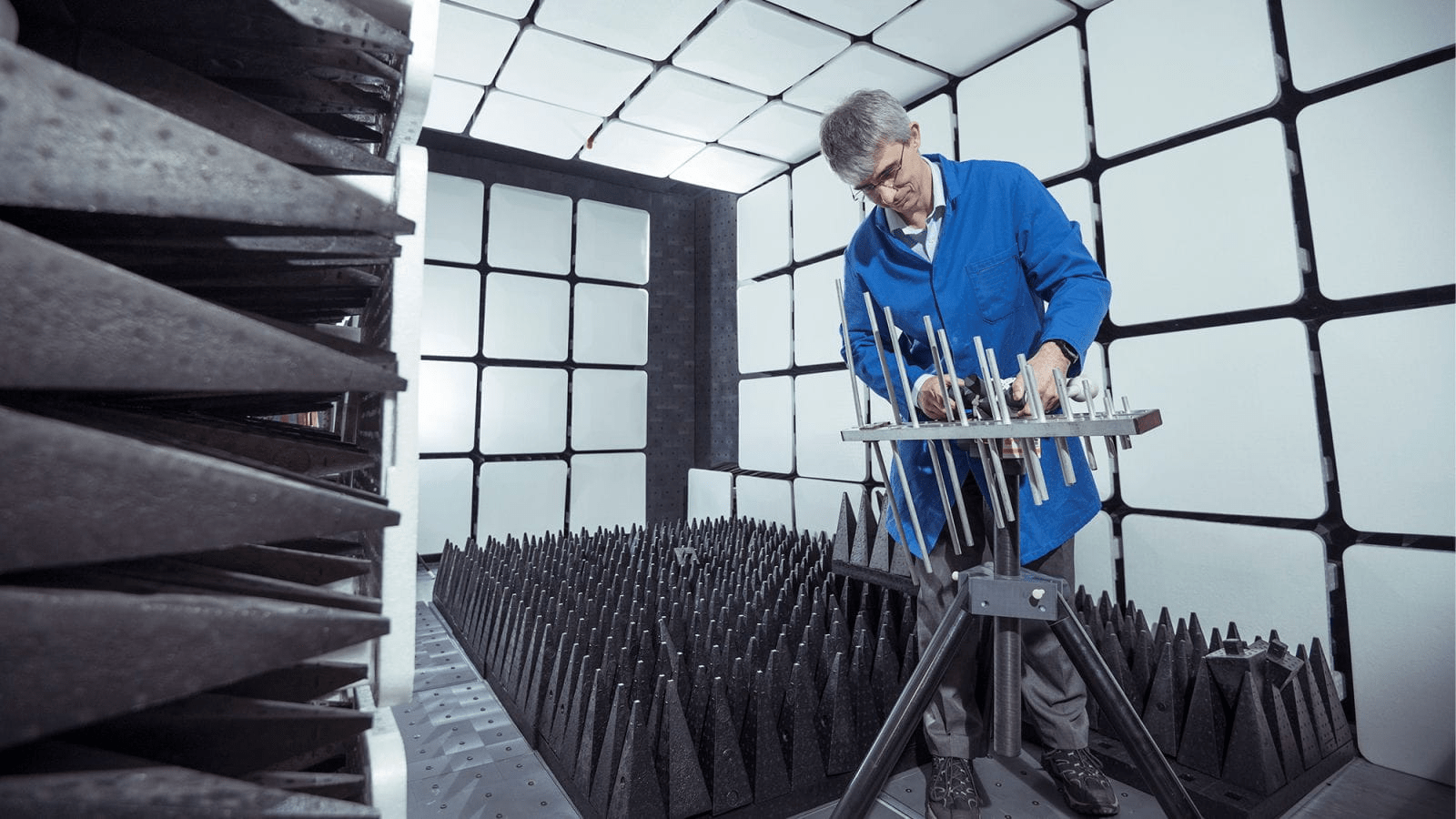 A man in a blue coat assembles an antenna in a small room