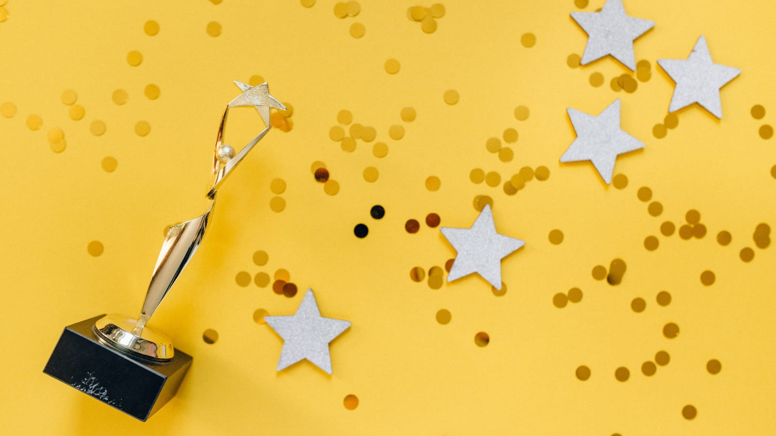 A golden award of a person holding up a star sits on a yellow surface surrounded by confetti