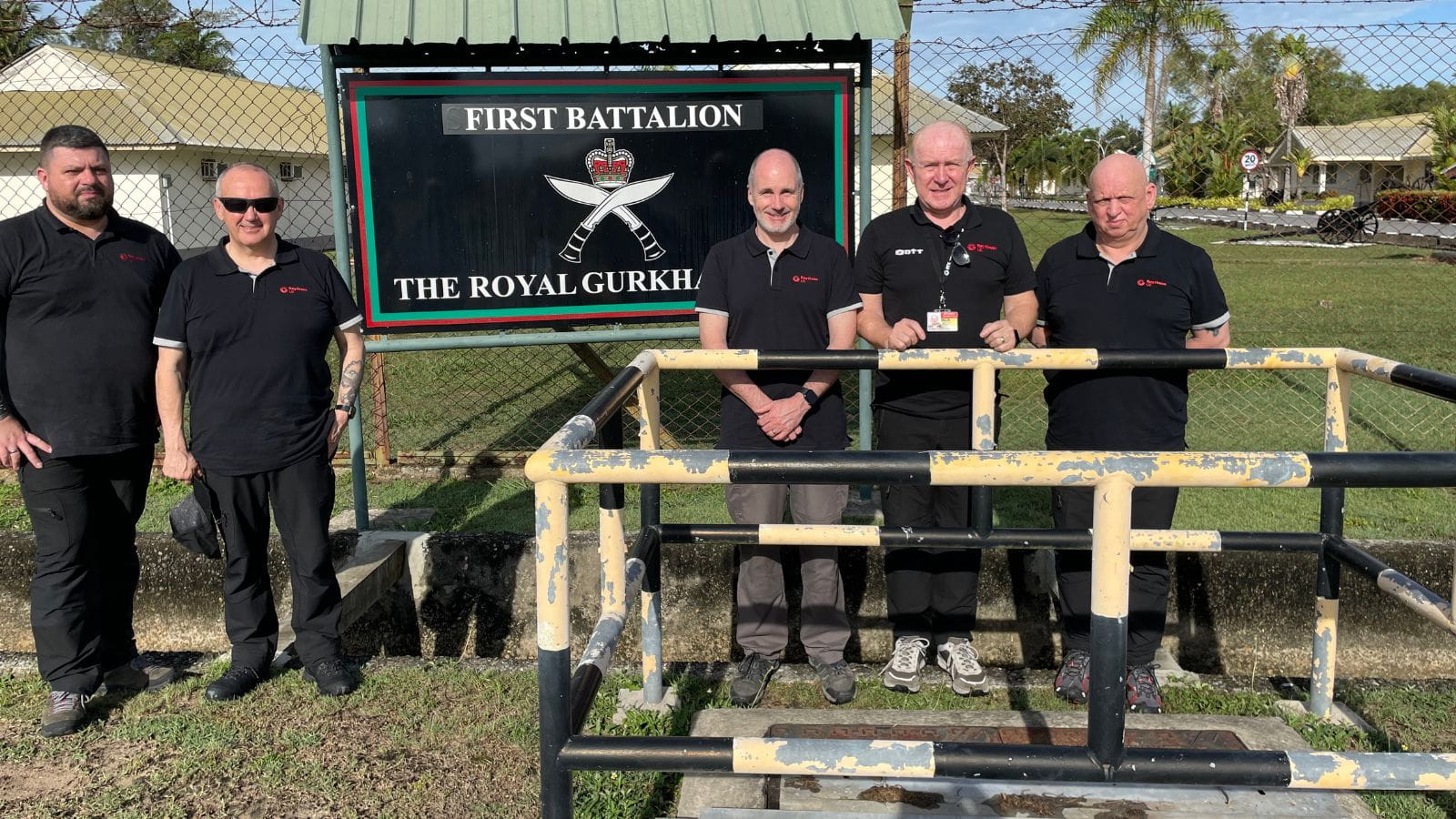 Raytheon UK team members stand in front of a sunny field outside the First Battalion Royal Guard in Brunai