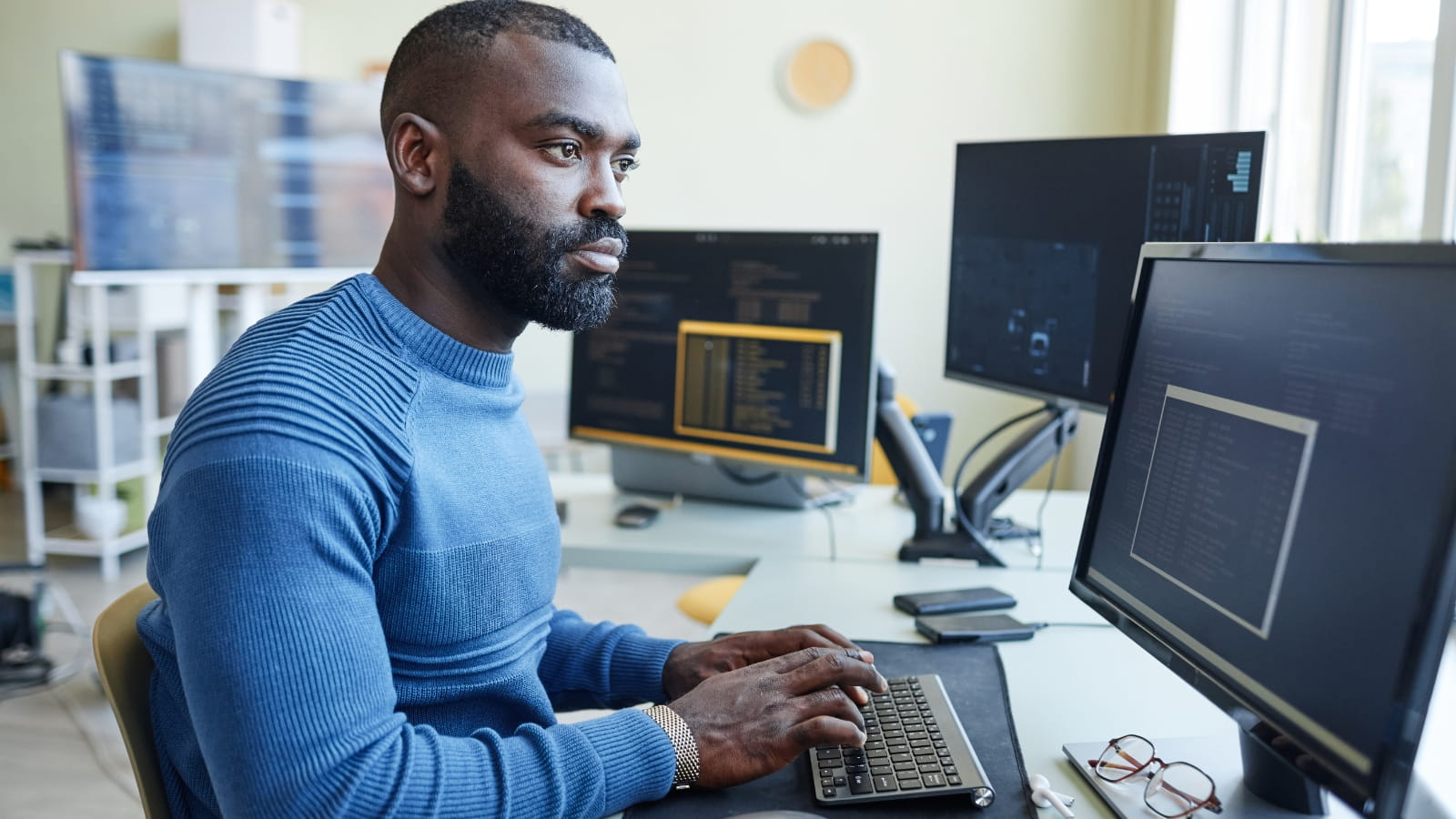 A software engineer works at three computer screens