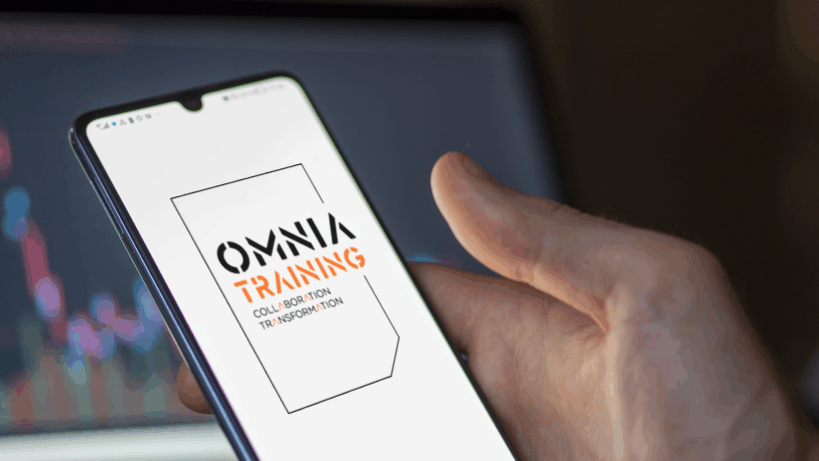 A hand holds a mobile phone. On the screen is the Omnia Training logo