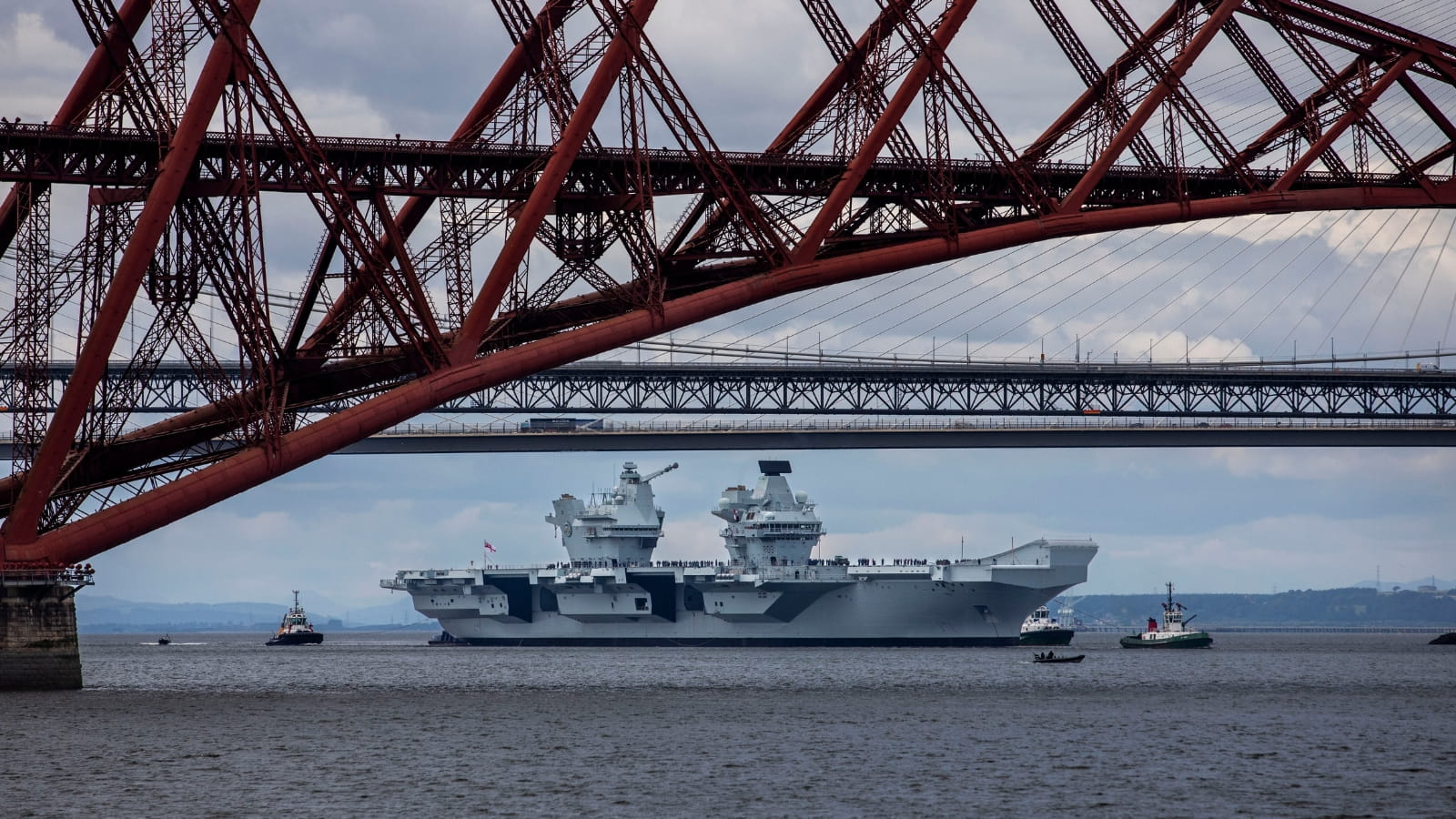 A navy ship sailing in the background with the forth bridge in the foreground