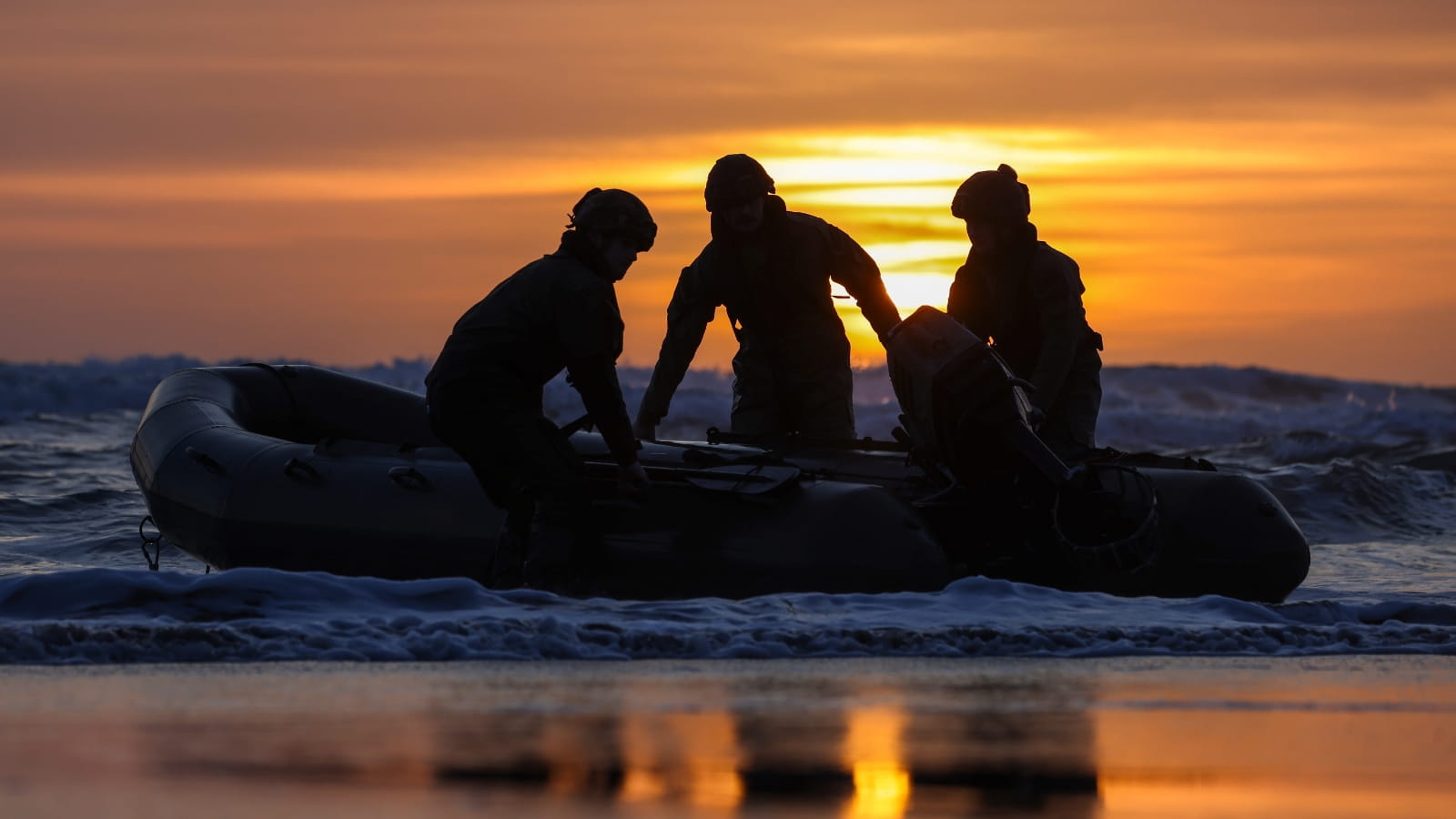 Commandos practice surf drills from an inflatable boat on shore at sunset