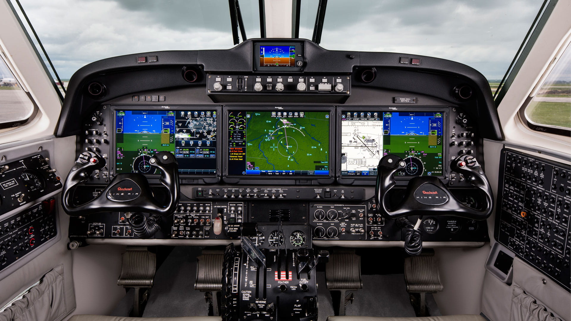 An aircraft flight deck. Three screens and two yokes are visible.