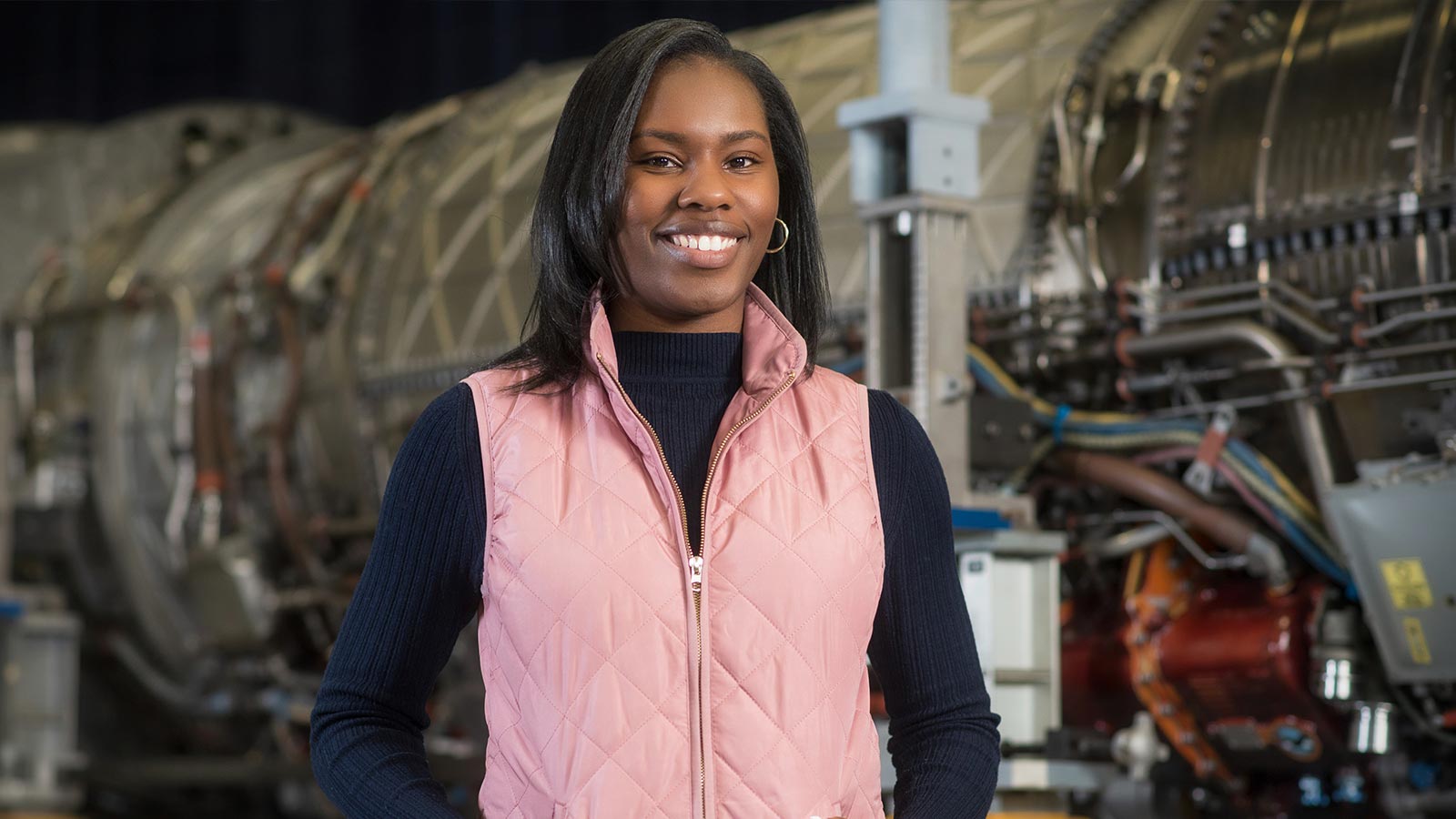 A young woman who is an engineer stands in front of an engine.