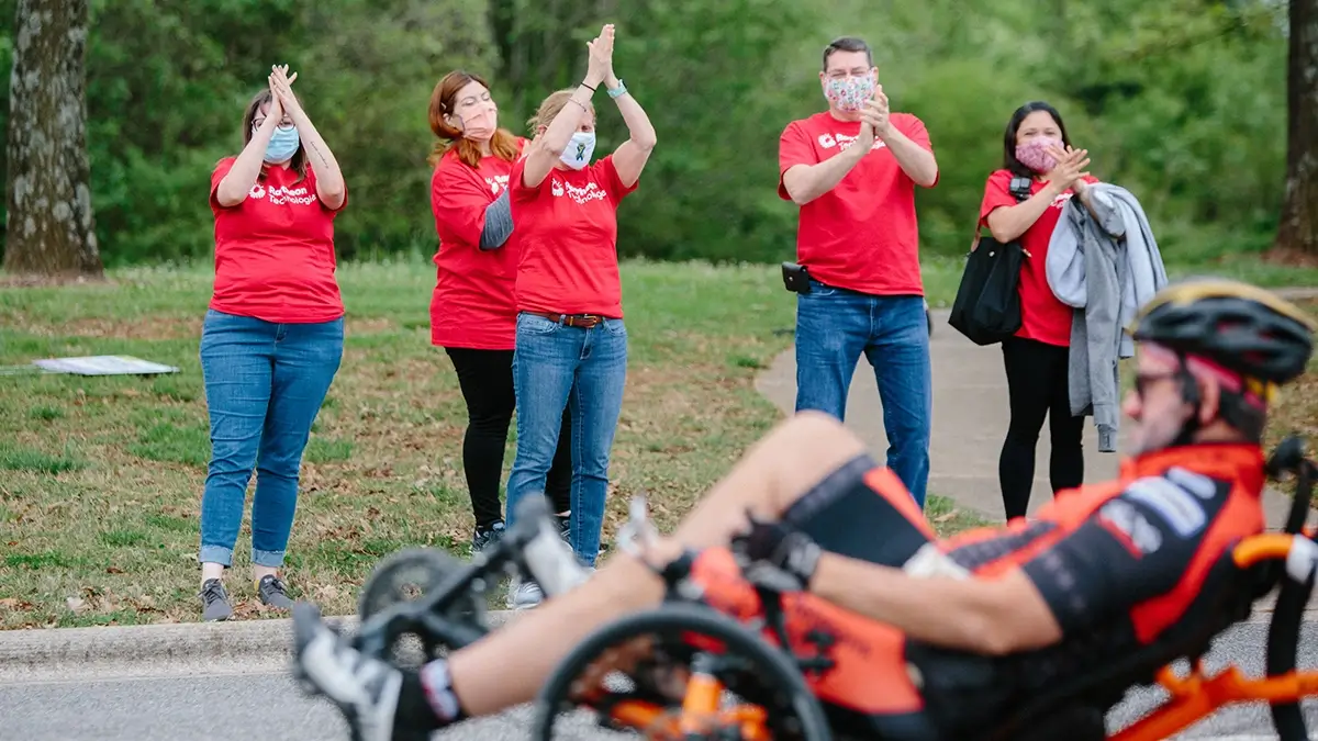 Paraolympian on a bike with Raytheon employees cheering him on