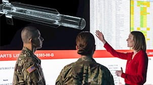 Two soldiers watching a presentation given by a woman about a missile