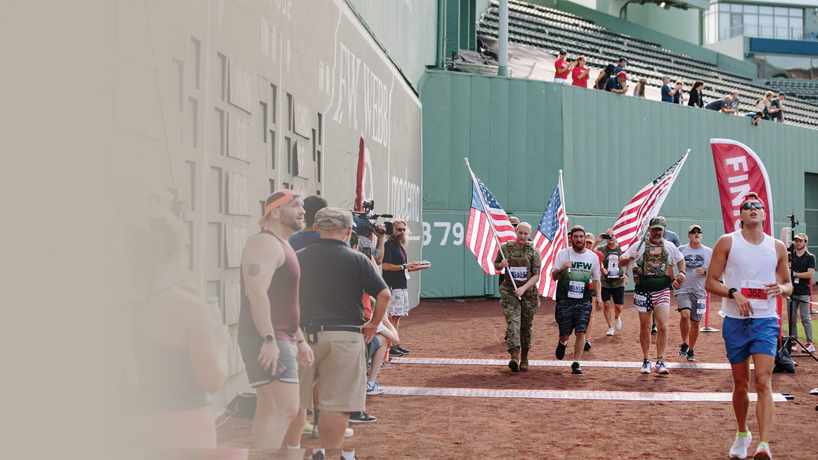 Three runners carry American flags during the Run to Home Base 9K event at Fenway Park in Boston.