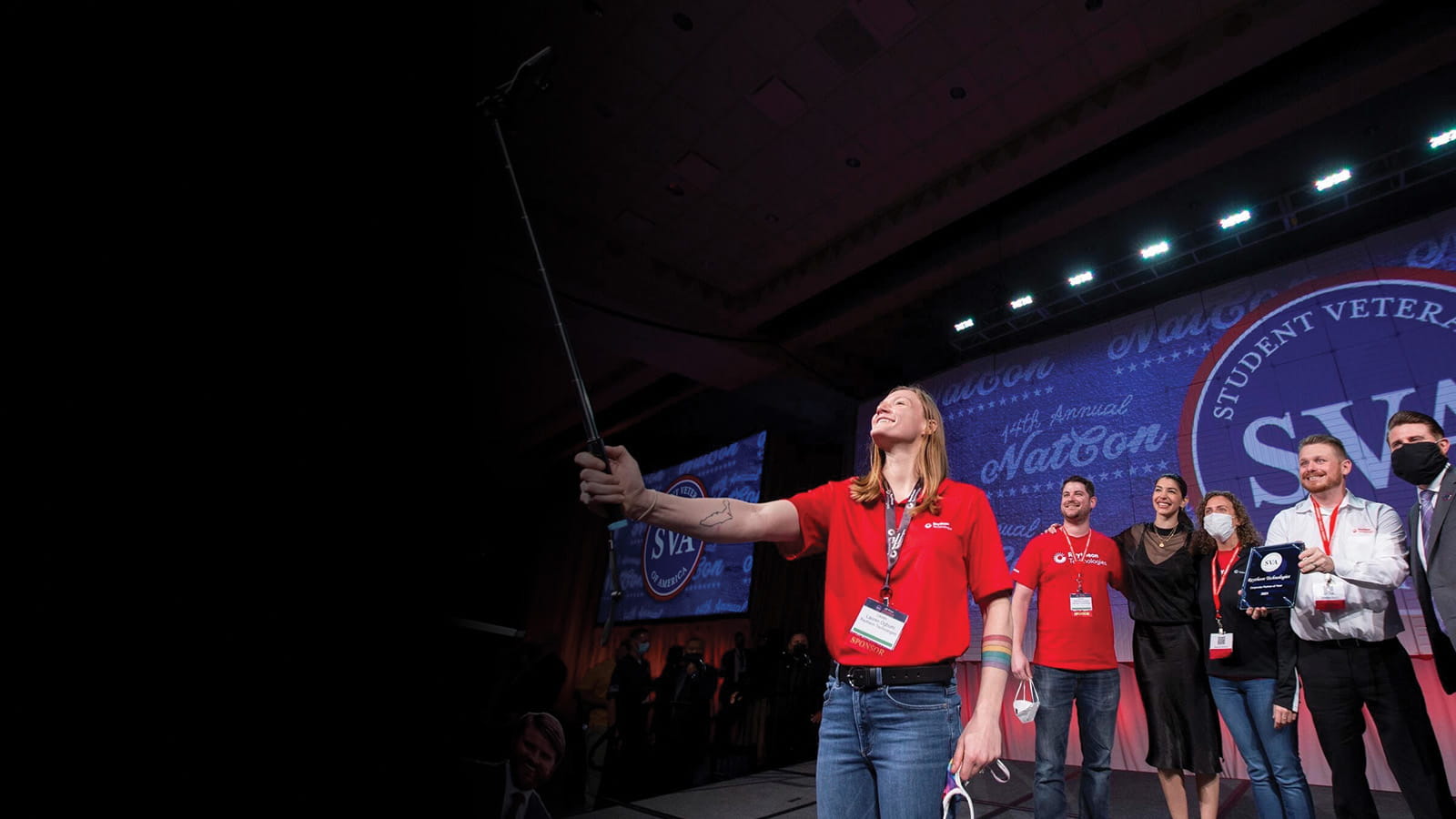A group of Raytheon Technologies employees uses a selfie stick to take a photo onstage with their Corporate Partner of the Year award at the Student Veterans of America national conference.