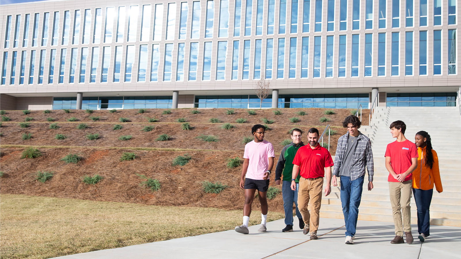 A group of students and a mentor from Raytheon Technologies walk together on the campus of the Alabama School of Cyber Technology and Engineering.