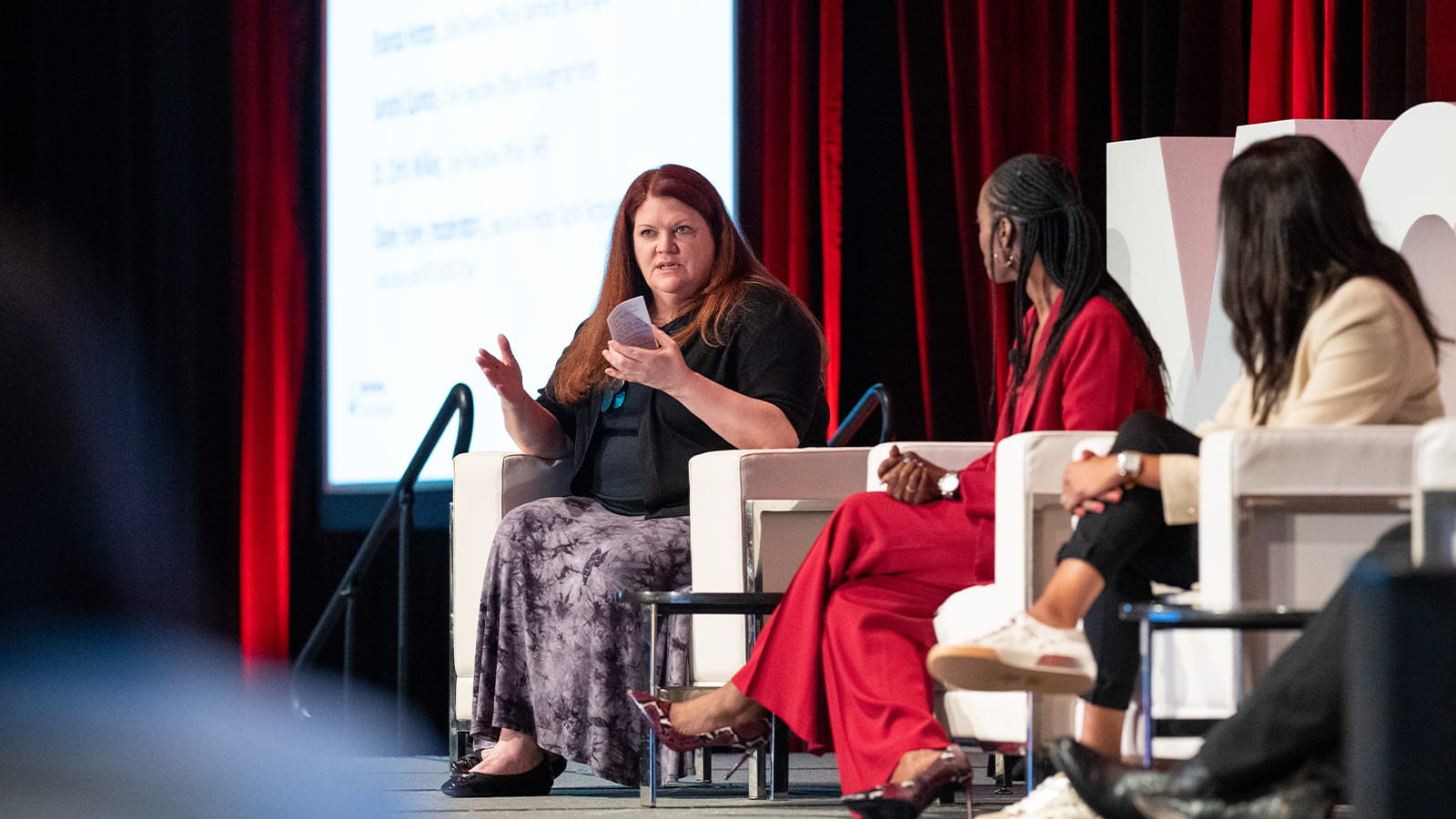 A woman in a white chair participates in a panel discussion onstage at a conference for leaders of employee resource groups.