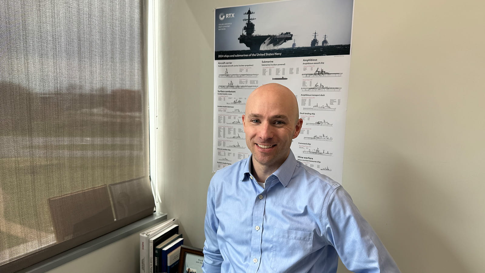 Cory Lloyd standing in front of Ships of the Navy calendar