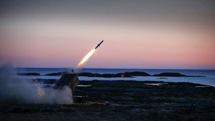 NASAM missile firing from a beach off into a twilight sky.