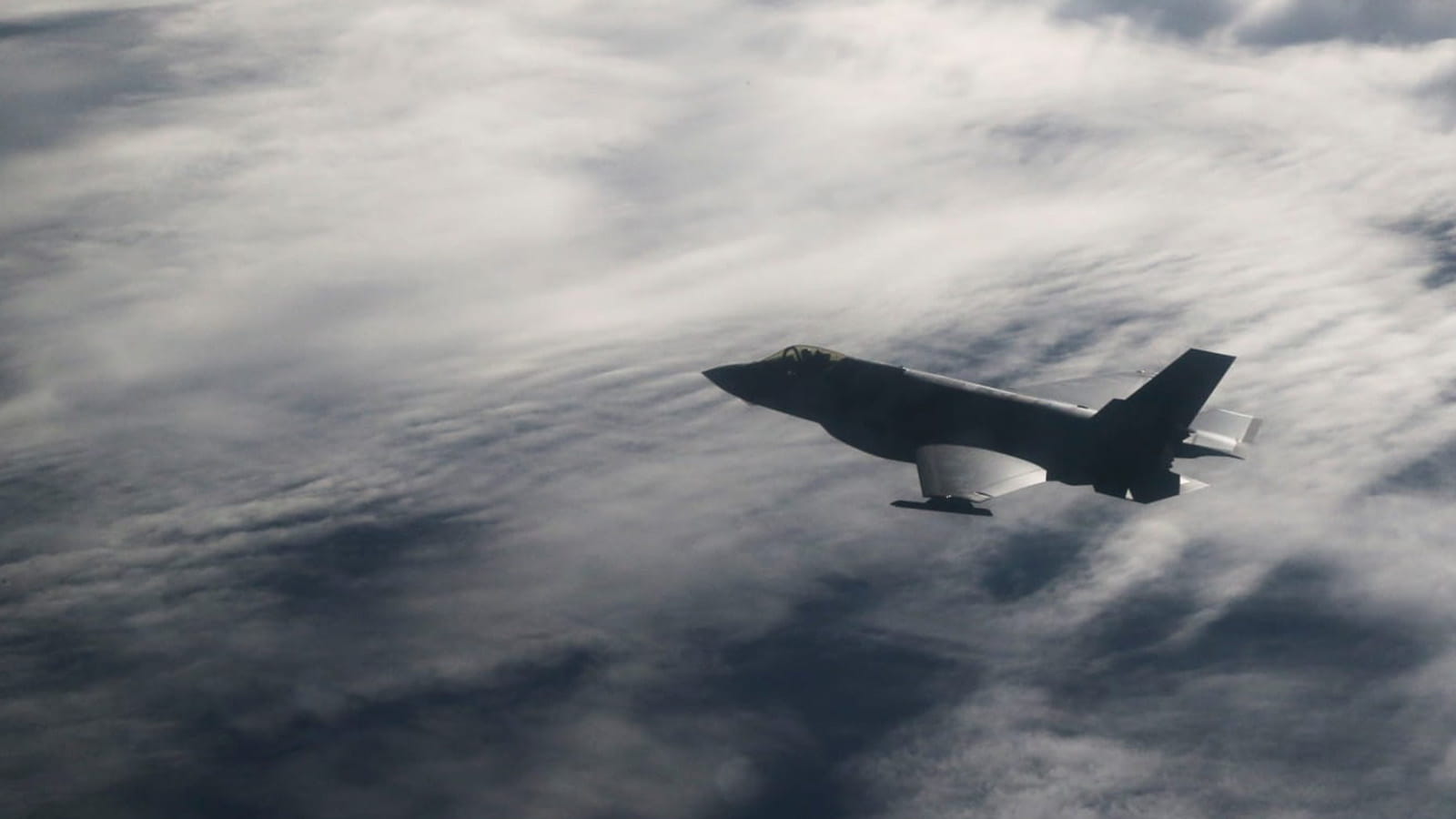 A fighter jet flying across a cloudy sky