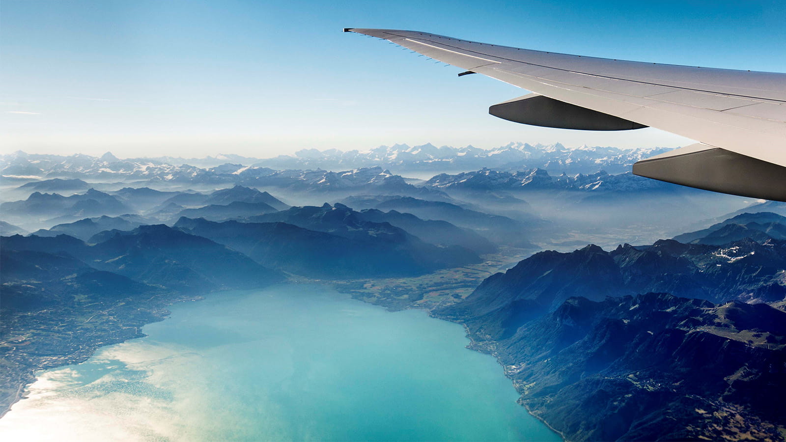 A side view of an airplane wing overlooking a lake and mountains