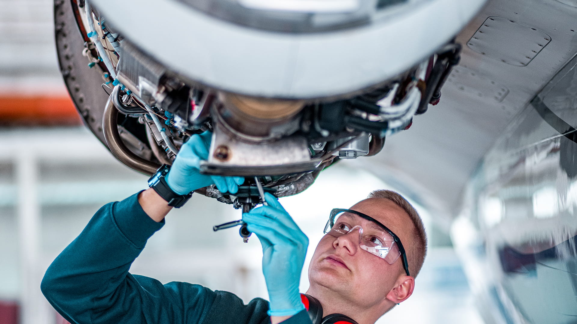 Adult male wearing safety glasses and blue rubber gloves working on an engine. 