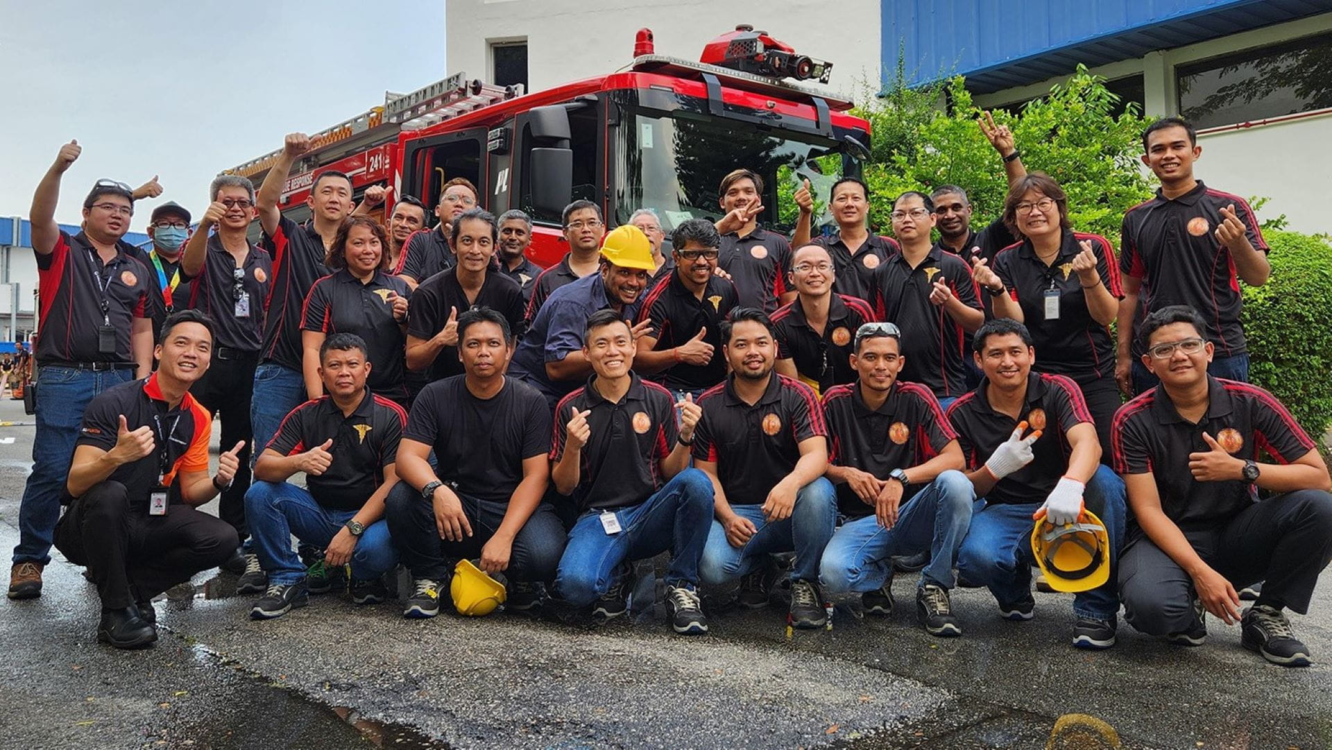 Group of adults wearing black and red shirts posing for a photo in front of a large red fire truck.