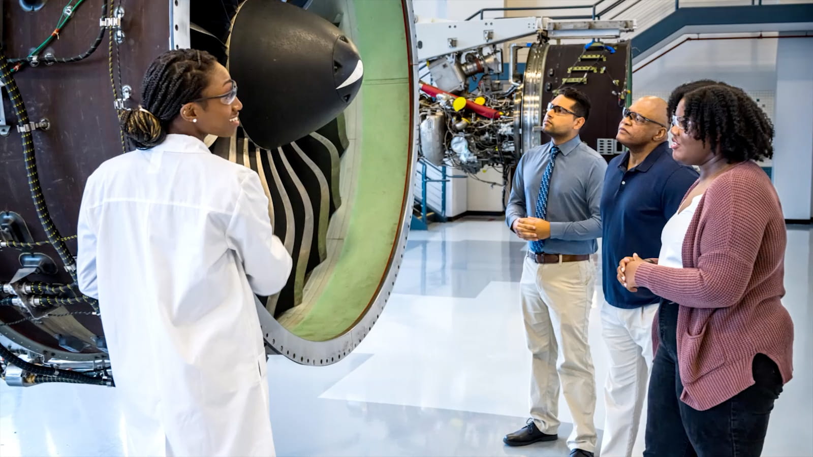 A worker explaining something about an aircraft engine to a group of workers