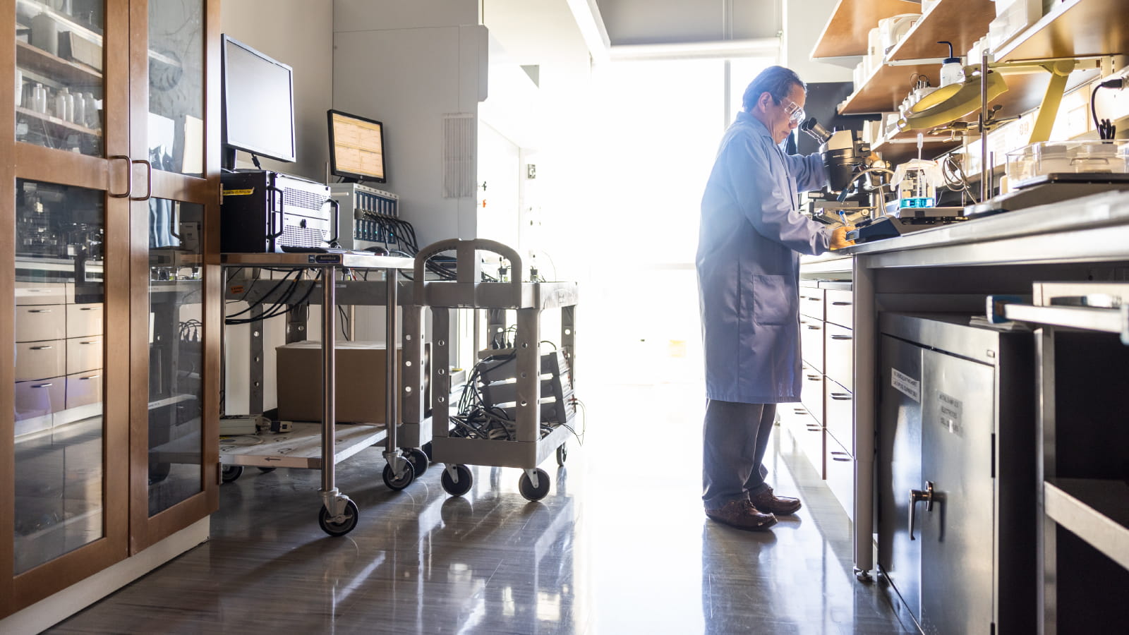 Man wearing lab coat looking into a microscope 