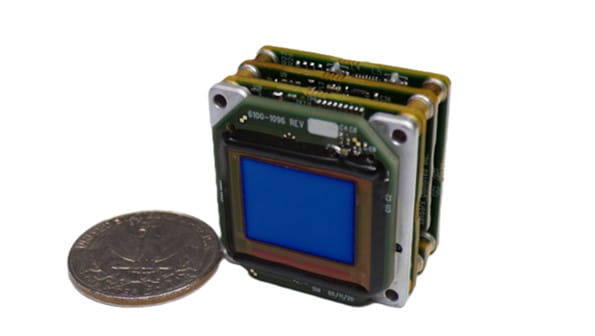 A Sensors Unlimited 1280JSX+MMT camera positioned next to a quarter, illustrating its small size