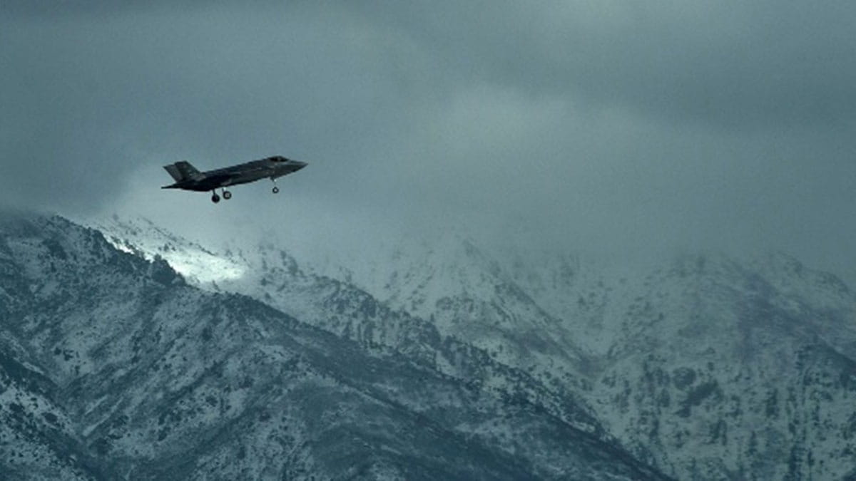 A fighter jet flying through foggy mountains