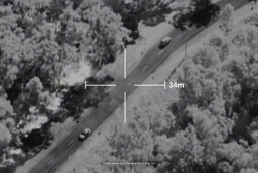 Two cars on a highway are visible through smoke using an infrared camera