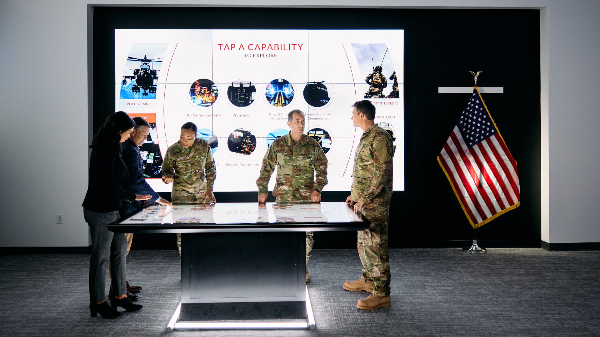Soldiers in camouflage and people in suits stand around an interactive table