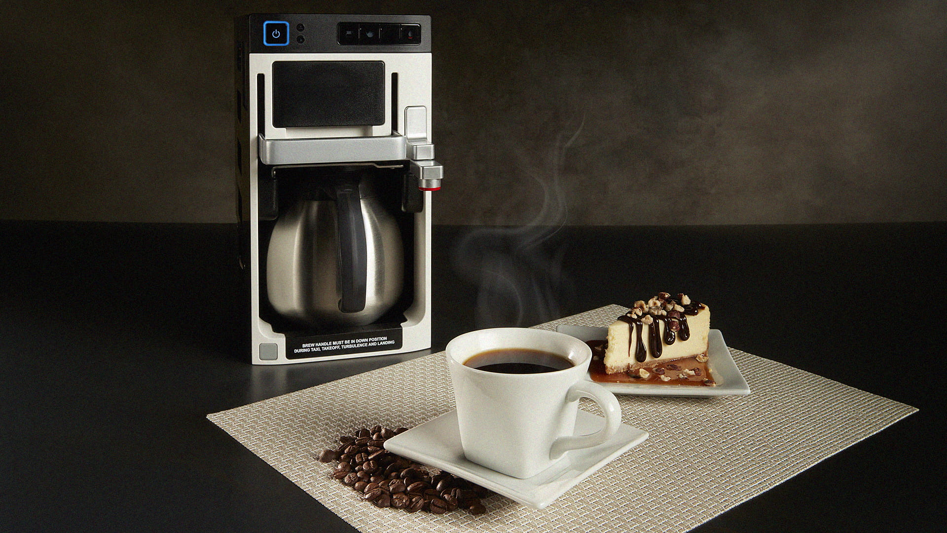 A coffee maker, a coffee cup, and a slice of cheesecake