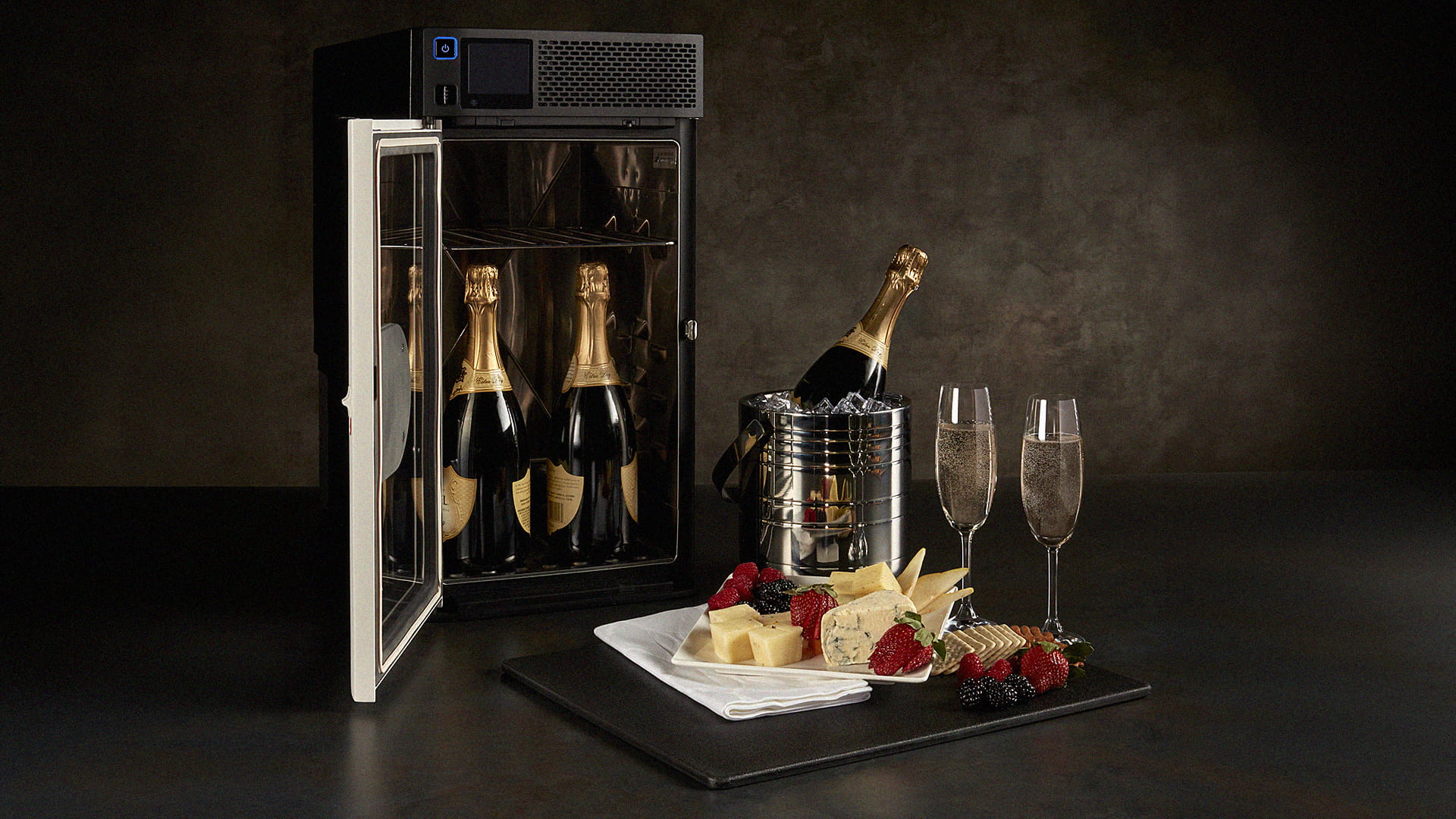 A beverage chiller with two bottles of wine inside, a dessert tray, a bottle of wine in an ice bucket, and two glasses of wine
