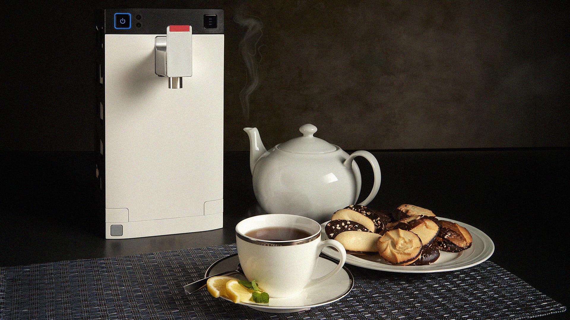 A small water heater for use on an aircraft, a teapot, a cup of tea, and a plate of pastries