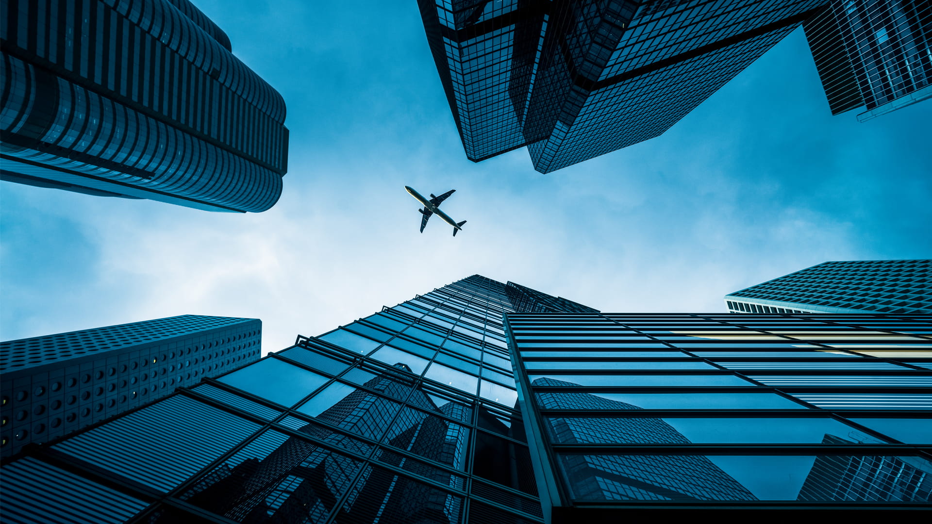 An airplane seen from the ground looking up between skyscrapers