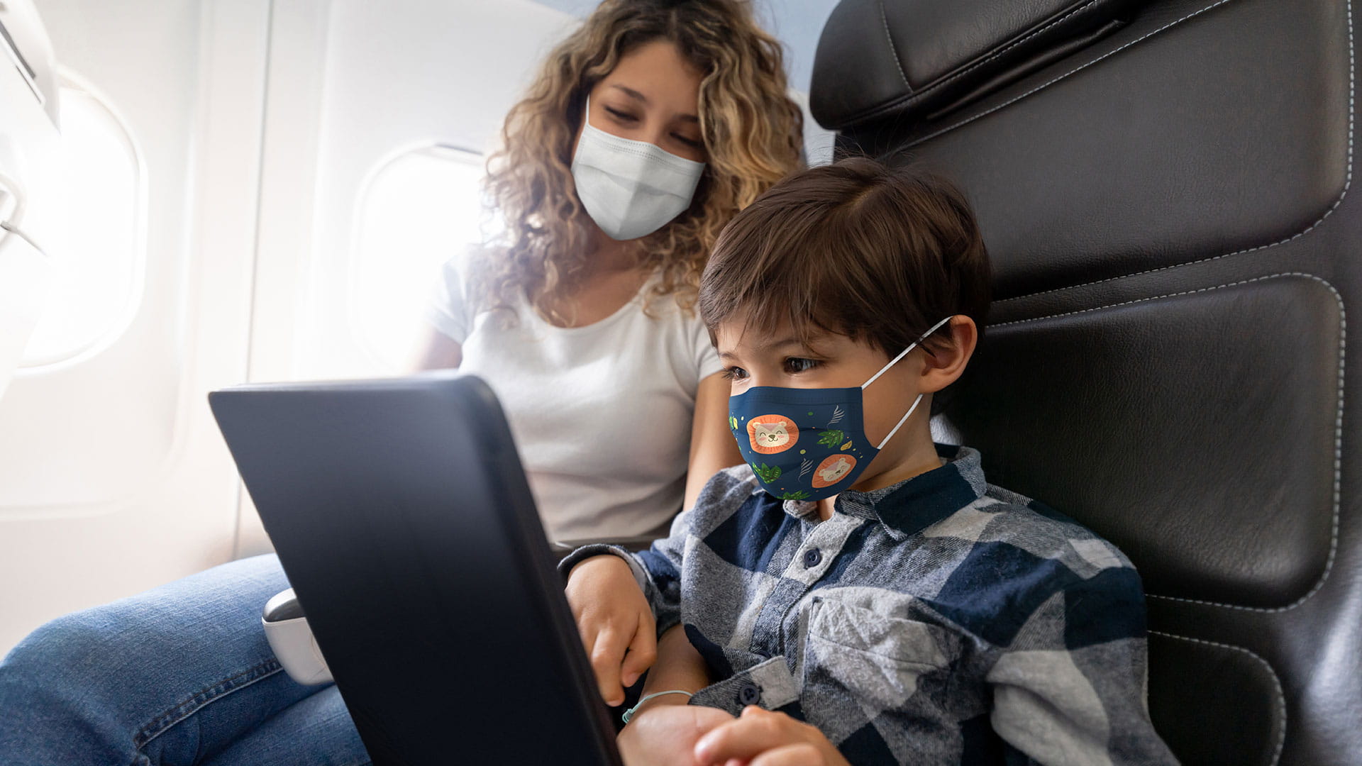 A mother looks on as her child uses a laptop