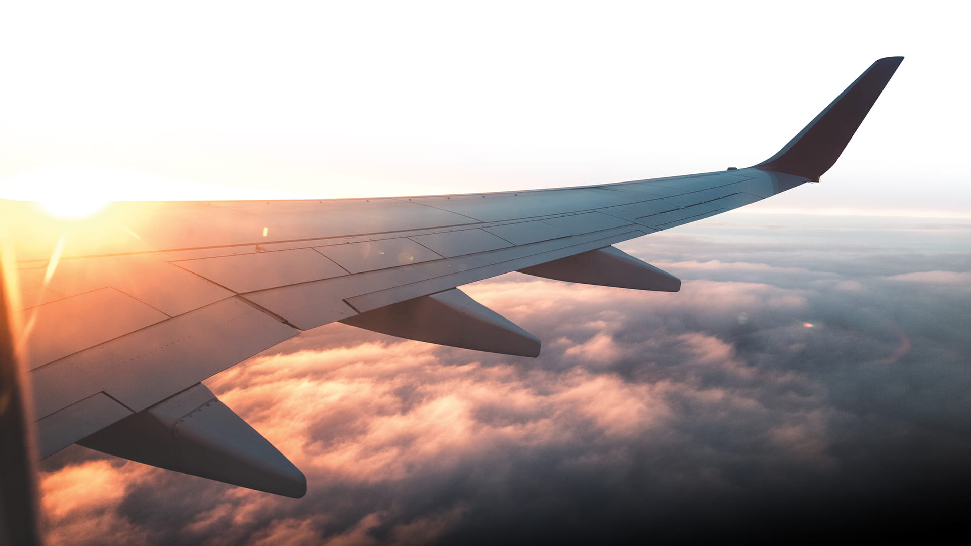 Photo of plane wing above clouds with sunset behind