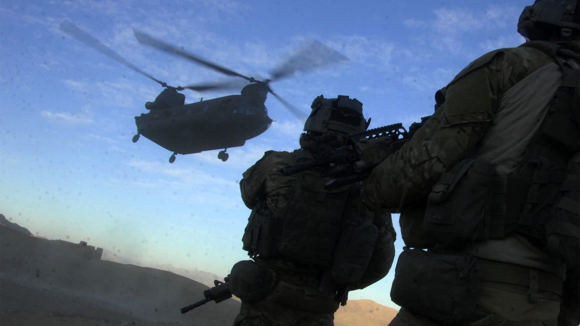 Military people holding rifles while watching military helicopter overhead