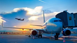 airplane on the tarmac and a distand airplane taking off into the sky