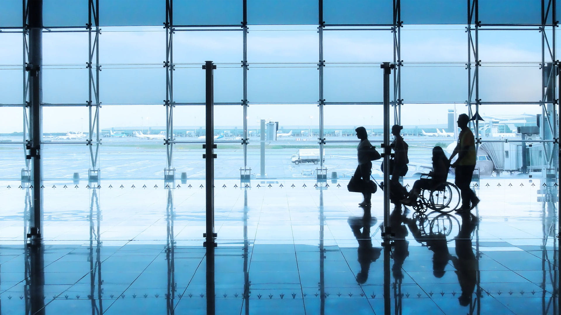 Four people walking through an airport. One is in a wheelchair.