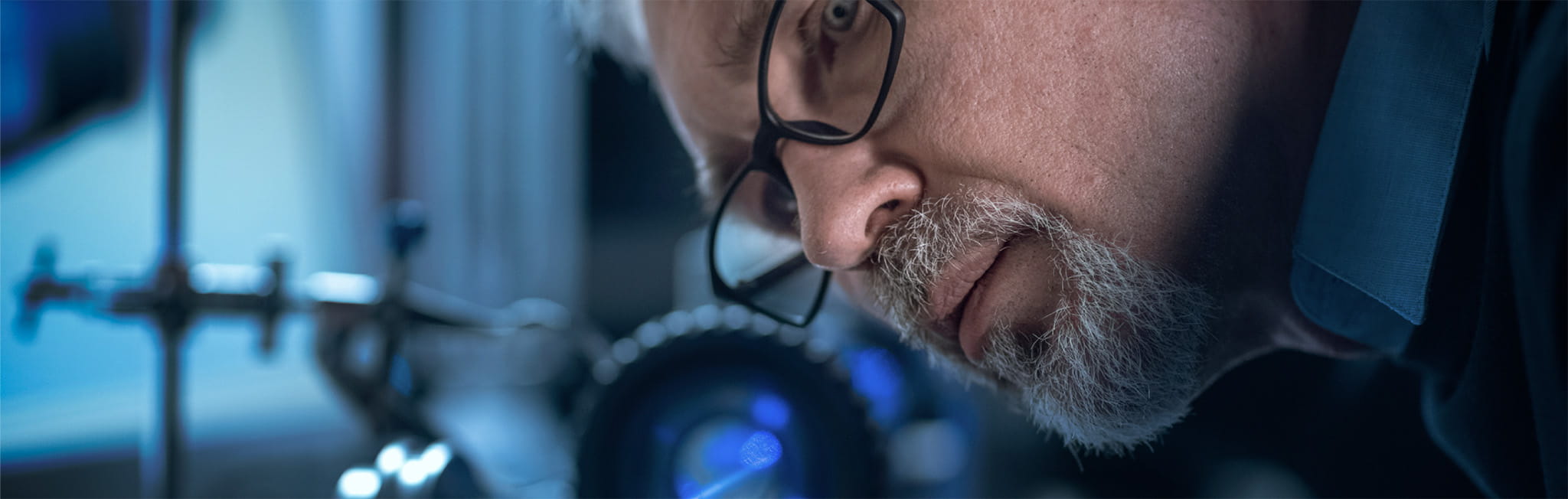 Engineer in glasses working with high precision laser equipment, using lenses and testing optics for accuracy required electronics